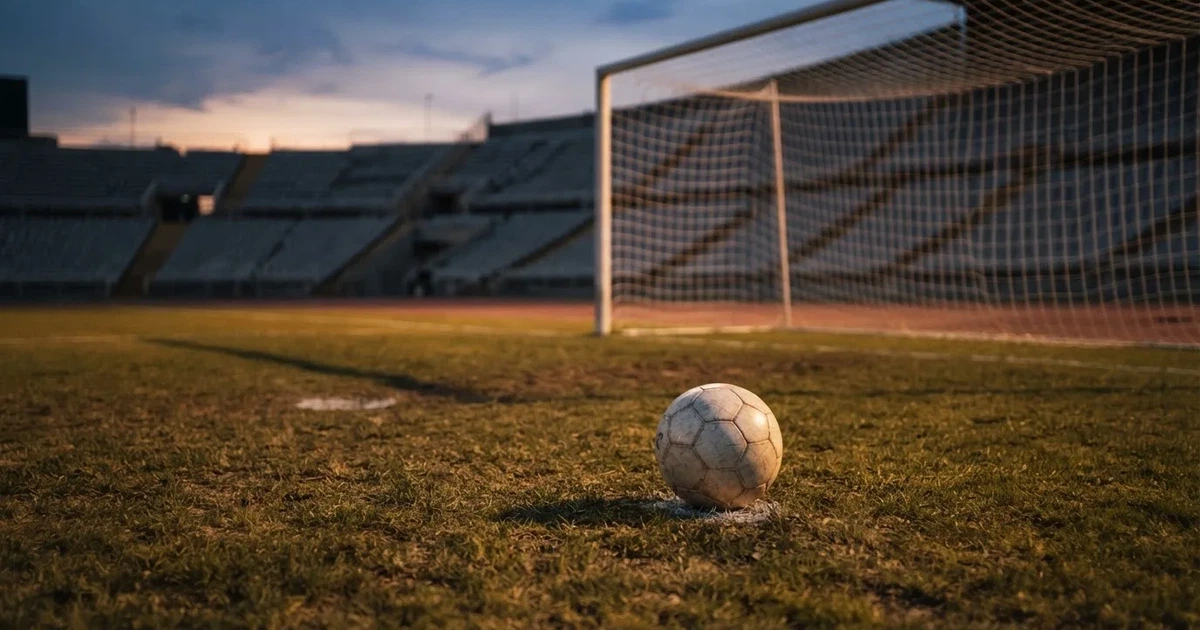 Ein Fußball liegt im Strafraum direkt vor dem Tor mit Netz, im Hintergrund leere Ränge bei Dämmerung.