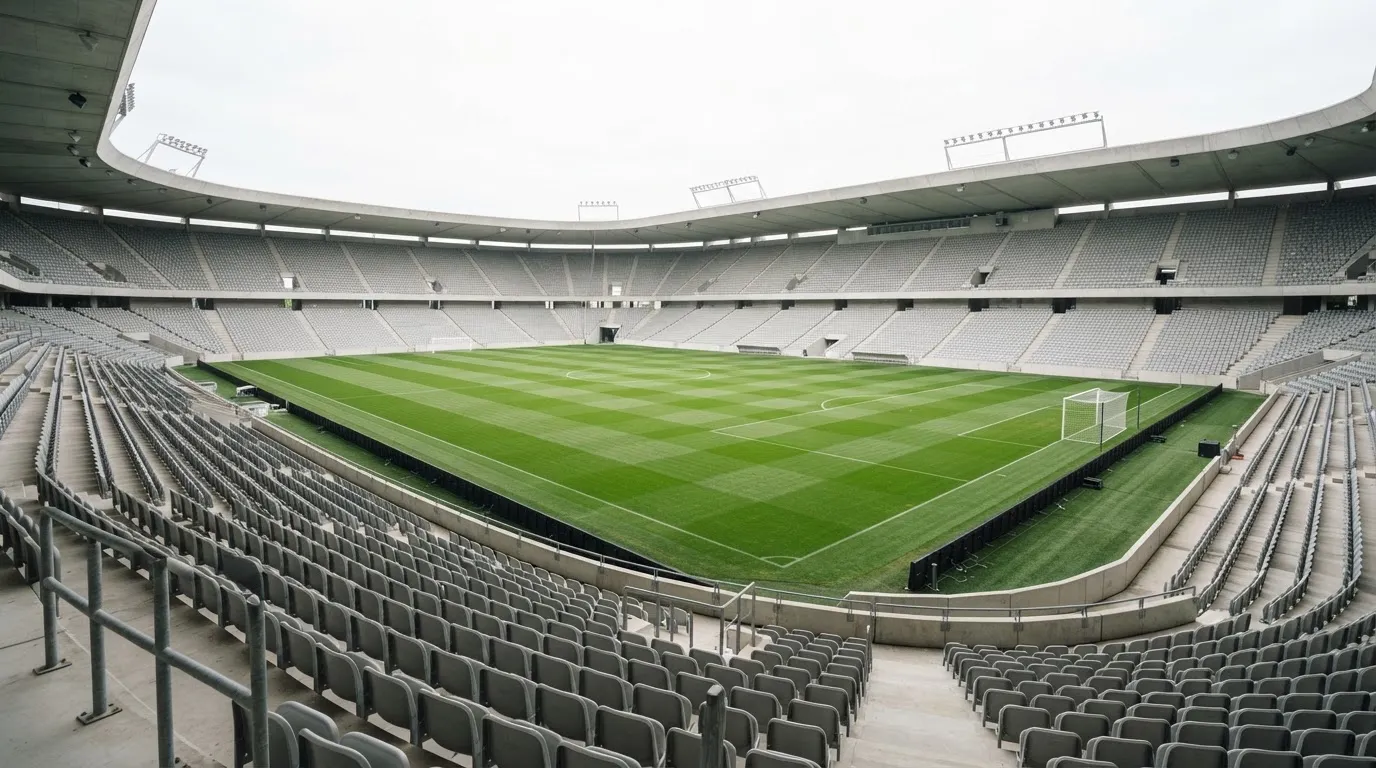Ein leeres Fußballstadion bei Tageslicht von der Tribüne aus gesehen, der Rasen zeigt gleichmäßige Mähstreifen.